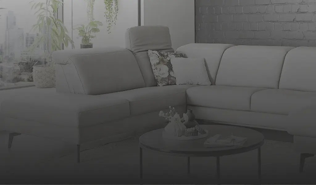 Stilvolles hellgraues Ecksofa mit verstellbaren Kopfstützen, gemütlichen Dekokissen und schwarzem Couchtisch im modernen Wohnzimmer mit Backsteinwand und Pflanzen. Perfekt für Wohnen mit Komfort und Design.